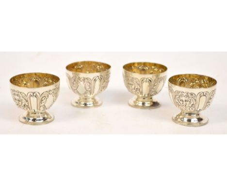 A set of four Victorian hallmarked silver egg cups embossed with alternating masks and shield shaped cartouches, with gilt wa