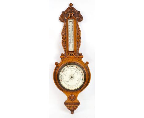 An early 20th century oak banjo barometer with circular dial below Centigrade and Fahrenheit thermometer, with carved scrolli