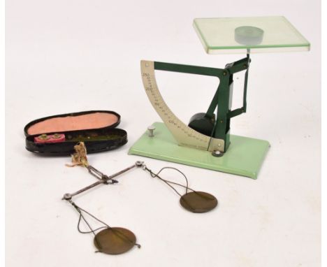 A cased pair of opium balance scales with small brass hands and two weights and a Production Posso scale on a tin plate plint