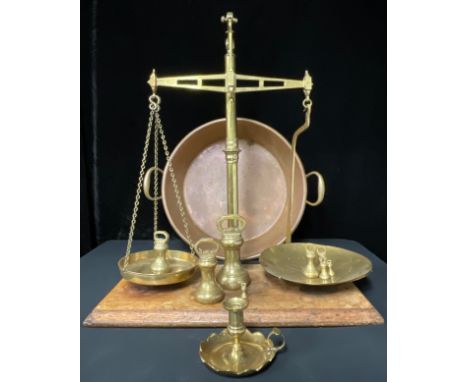 A set of brass balance scales; a set of graduated brass bell weights; a large copper two-handled pan; a brass chamber stick 