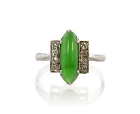 A jade and diamond dress ring in white gold or platinum set with a central elongated oval cabochon cut piece of green jade fl