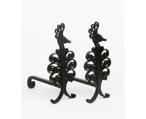 A pair of patinated wrought iron fire dogs in the manner of Edgar Brandt, tripod base with scroll feet, the stem with ornate 