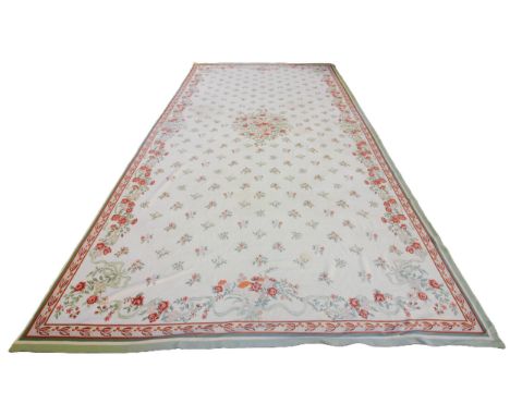 A large Portuguese needlepoint carpet, the central floral medallion upon an ivory coloured ground punctuated with conforming 