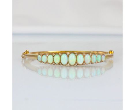 A late 19th/early 20th century opal and diamond bangle, the eleven graduated cabochon opals with rose cut diamond highlights,