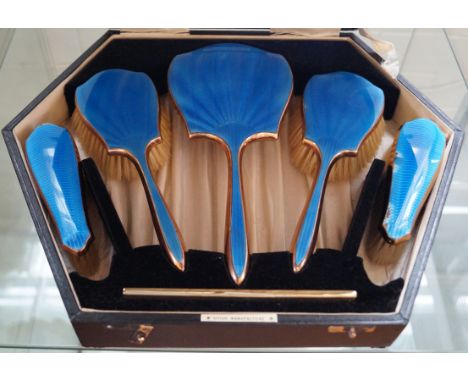 An excellent quality cased six piece blue enamel backed dressing table set comprising, comb, hand mirror, two clothes brushes