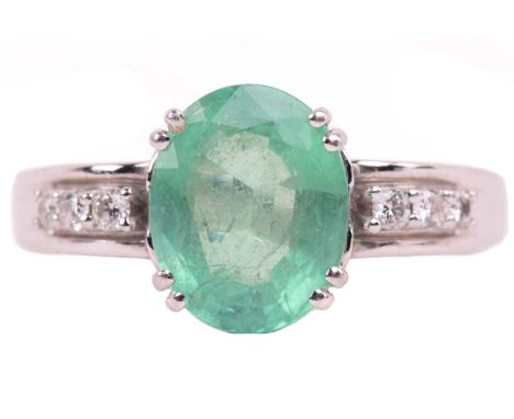 An emerald and diamond dress ring in platinum, consisting of an oval-cut emerald with pale green body colour, in double claw 