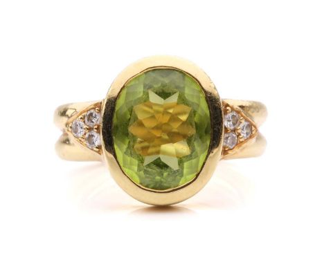 A peridot and diamond dress ring, collet-set with an oval-cut peridot of 12.0 x 9.4 x 5.4 mm, flanked by two diamond-set tria