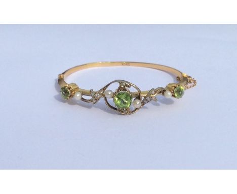 A large peridot and pearl hinged bangle with swirl decoration and concealed clasp with safety chain. Approx. 11 grams. Est. £