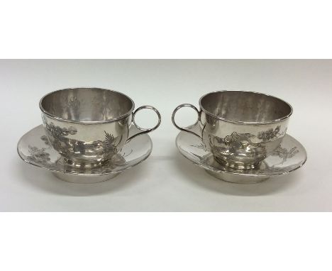 A pair of unusual Chinese silver cups and saucers decorated with birds and foliage. Approx. 292 grams. Est. £200 - £300.