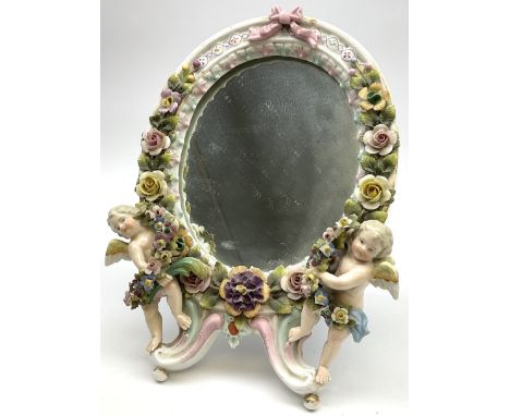 A late 19th century Sitzendorf mirror, the floral encrusted frame with two applied cherubs, with easel style support verso, a