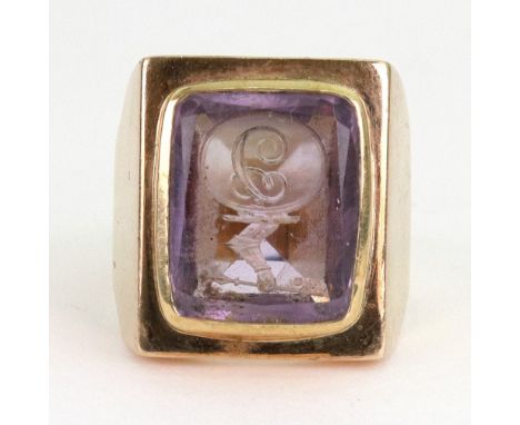 An amethyst intaglio signet ring, the rectangular intaglio carved with a letter 'J' and crest, rub-over set in a wide shank, 