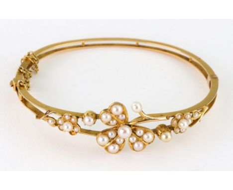 An Edwardian gold and half-pearl hinged bangle, the open front designed as a flower-head trefoil between smaller flower and s
