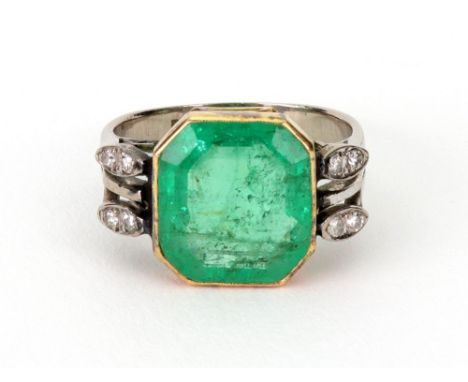 An emerald and diamond ring, the large step-cut emerald, rub-over set in yellow metal between four stone diamond shoulders, s