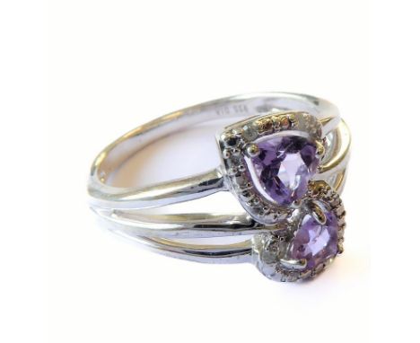 A hallmarked silver dress ring in a crossover design, centrally set with two opposing heart-shaped pale amethysts surrounded 