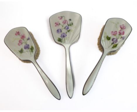 A lady's three-piece, hallmarked-silver and enamel dressing table set comprising hand-held mirror and two hair brushes,&nbsp;