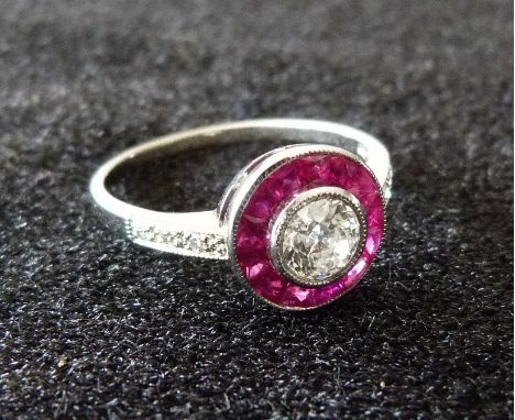 An 18ct. White Gold Art Deco Style Ruby and Diamond Ring, with a central diamond surrounded by rubies and with diamond should