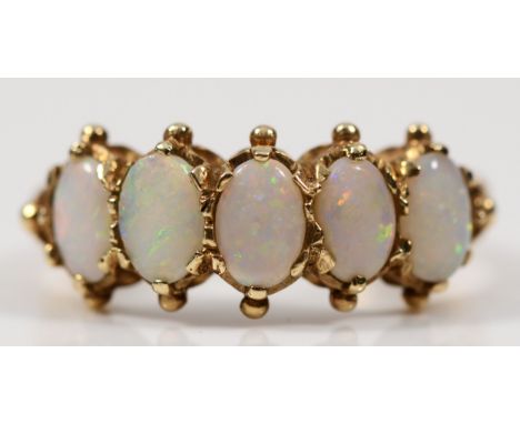 A 9ct gold five stone opal dress ring, with pierced scrolling shoulders, the opals showing flashes of red, orange, blue and g