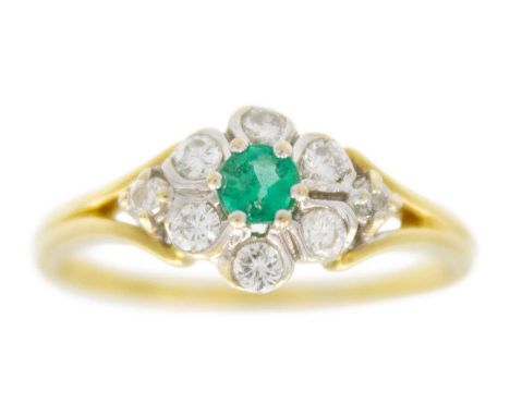 A modern 18ct diamond and emerald set cluster ring. The central round cut emerald of 0.20ct estimated weight, surrounded by s
