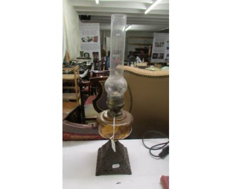An old oil lamp on iron base with amber coloured glass font and chimney. COLLECT ONLY.