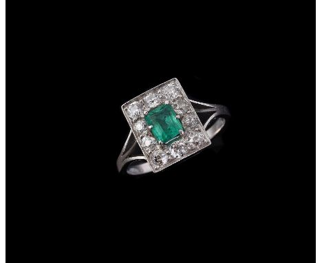 A mid 20th century diamond and emerald cluster ring, the central step cut emerald with canted corners, within a surround of o