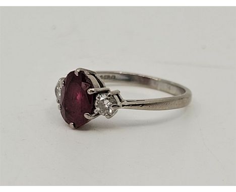 An 18ct. white gold ruby and diamond ring, set mixed oval cut ruby to centre flanked by single round brilliant cut diamond to