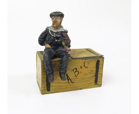 An Early 20th Century Figural Match Striker of a lead sailor sitting on a tin 'Fire' Trunk 