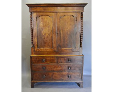 A George III Oak and Mahogany Welsh Bacon Cupboard, the moulded cornice above two shaped panelled doors flanked by spiral pil