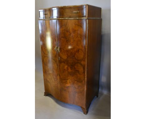 An Art Deco Walnut Serpentine Side Cabinet with a frieze drawer above two doors enclosing drawers, raised upon shaped bracket