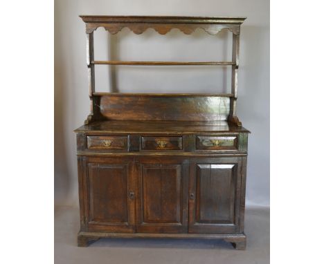 A George III Oak Dresser, the open shelf back above three drawers and two cupboard doors with central panel raised upon brack