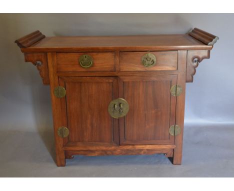 An Early 20th Century Chinese Hardwood Altar Table, the scroll end top above two drawers and two cupboard doors, raised upon 