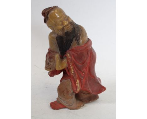 A Chinese soapstone carving, of Shou Lao, clutching the peach symbolic of longevity, wearing a flowing robe incised with scro
