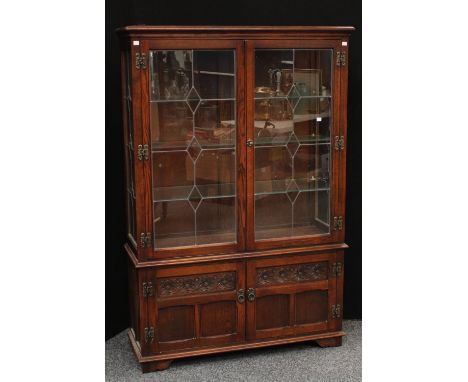 An Old Charm oak display cabinet, moulded cornice above a pair of glazed doors enclosing three shelves and a pair of panel do