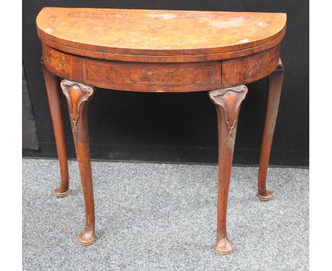 A Queen Anne style walnut demilune card table, folding top enclosing a baize lined playing surface, above a frieze drawer, st