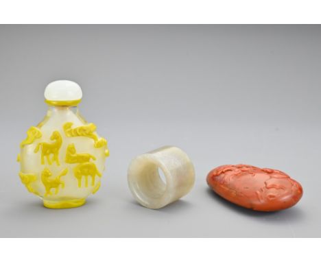 A Chinese glass snuff bottle with yellow figures of horses and clouds in relief. Together with a jade thumb ring and red ston