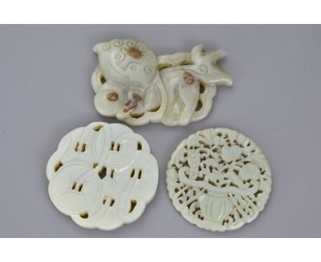 A Chinese pale celadon pendant in buckle form carved as a lion dog playing with a ball together with two circular jade pendan