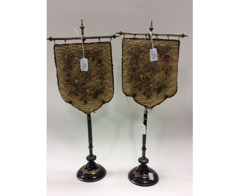 A pair of Victorian table top pole screens, silk backed woolwork panels, black glazed ceramic stands, height 52cm (2)
