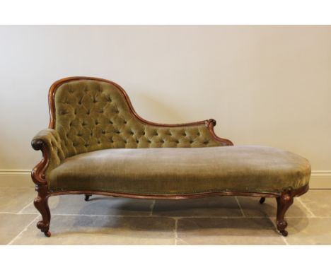 A Victorian mahogany framed and green velour chaise lounge, the arched button back extending to a carved paper scroll termina