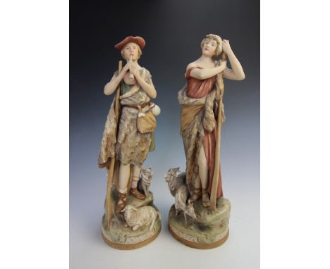 A pair of Royal Dux models of a Shepherd and Shepherdess, modelled with he playing a pipe besides a dog and she supported by 