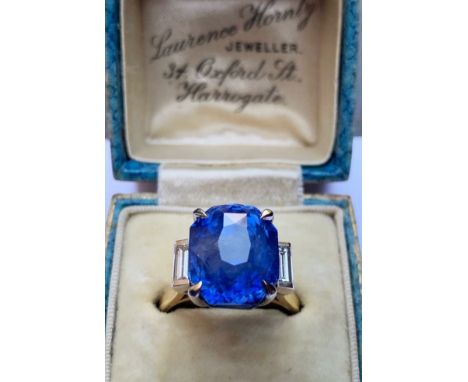 A sapphire and diamond ring, the central octagonal mixed cut transparent blue sapphire claw set with a baguette cut diamond t