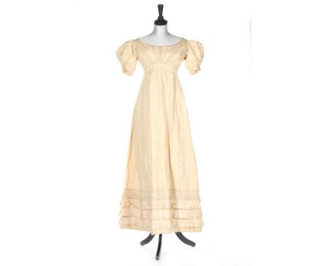 An ivory silk evening dress, circa 1820, empire line with puff sleeves, the bodice adorned with frond-like piping, triple tie