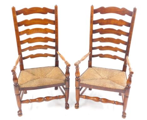 A pair of oak six rung ladder back country chairs with rush seats, raised on turned legs united by turned stretchers.