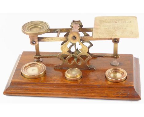 A set of early 20thC brass postal scales, with weights, raised on an oak base, 31.5cm wide.