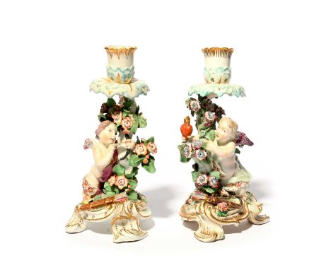 A pair of Chelsea candlestick figures, c.1765, each modelled with a winged putto or Cupid, one drawing back an arrow in a bow