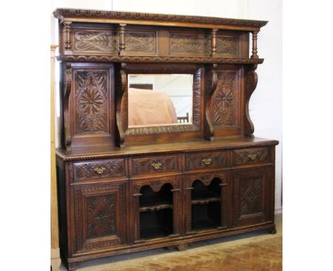 A Victorian carved oak dresser, with elaborate single shelf mirror back above four drawers, two cupboards and two open shelve