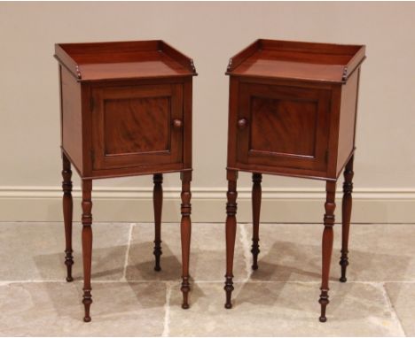 A pair of 19th century mahogany bedside cupboards, each with a three quarter gallery above a single panelled door, raised upo