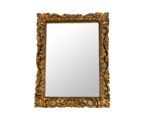 A late 19th century rococo revival giltwood wall mirror, the plain rectangular plate within a frame moulded with scrolling ac