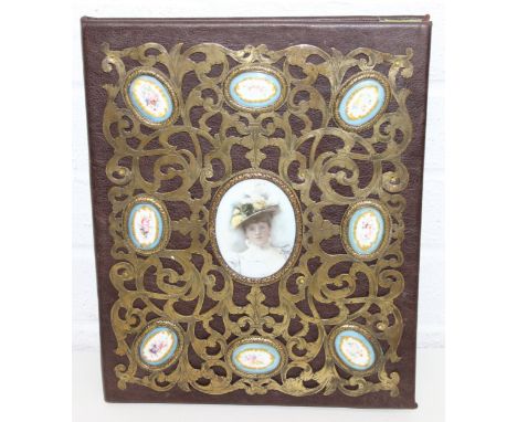 An antique or vintage leather covered blotter set with a fretwork brass panel to front, porcelain vignettes of flowers surrou