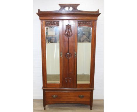 An early 20th century mahogany wardrobe with carved Art Nouveau motifs, mirrors to side, carved panel to to centre and deep d