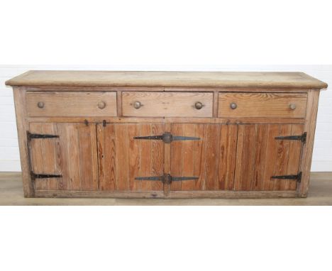 A large antique pine dresser base comprising of three deep drawers with turned handles over four cupboard doors, 19th century