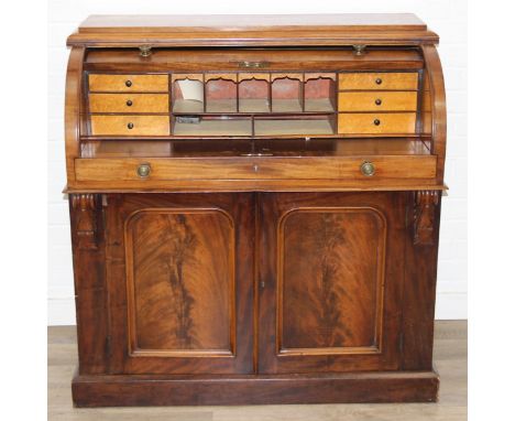 A Victorian mahogany rolltop desk with fitted interior above a cupboard, plinth base, brass mounts, 109cm x 55cm x 110cm